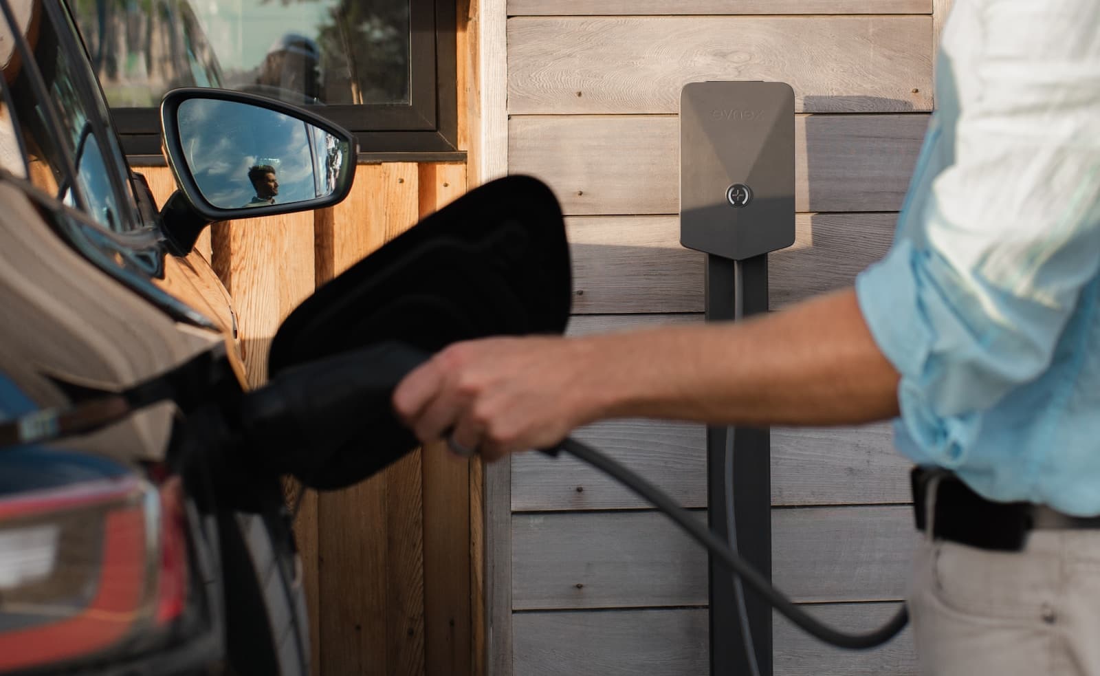 A driver plugging a charging cable into an electric car beside a home wall charger