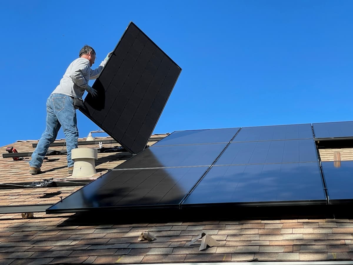 An installer fitting solar panels onto a residential shingle roof