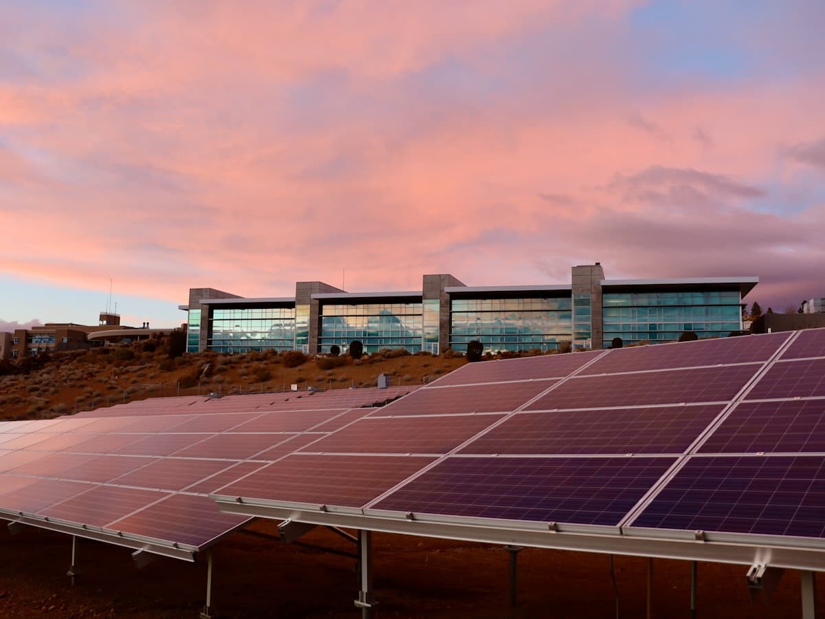 Solar panels in front of a modern glass office building at sunset